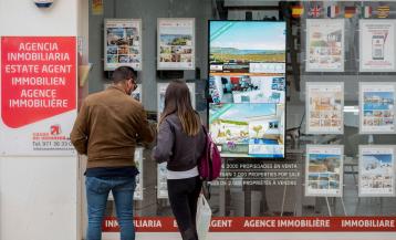 Dous mozos miran as ofertas dunha axencia inmobiliaria