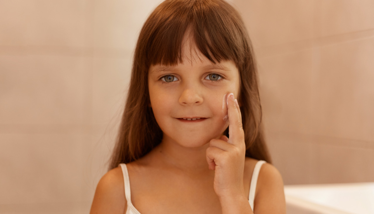 Toma en interiores de una nina con crema facial en la mejilla senalando con el dedo en la cara mirando directamente la camara vistiendo una camiseta blanca sin mangas realizando procedimientos de belleza sola